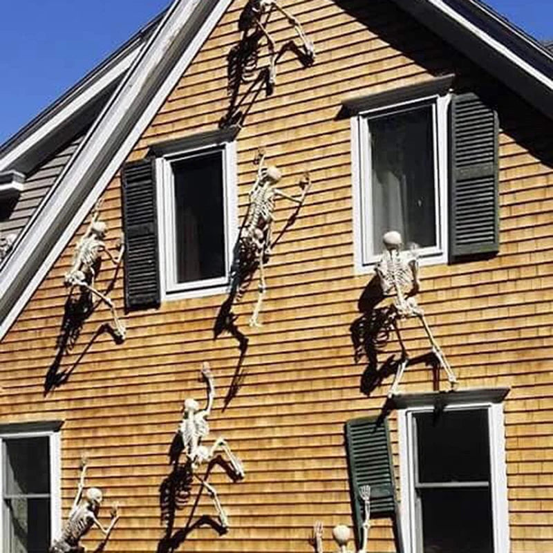 Multiple white hanging skeleton props on the side of a house for Halloween