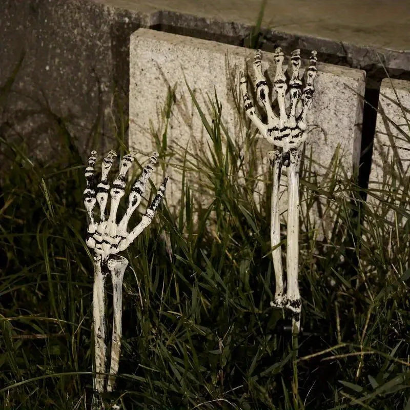 Skeleton hand garden stakes standing in front of a stone wall, white-gray finish