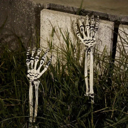 Skeleton hand garden stakes standing in front of a stone wall, white-gray finish